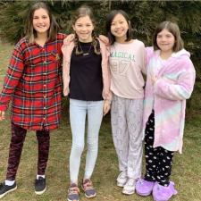 Four female students pose for a picture outside in front of a tree